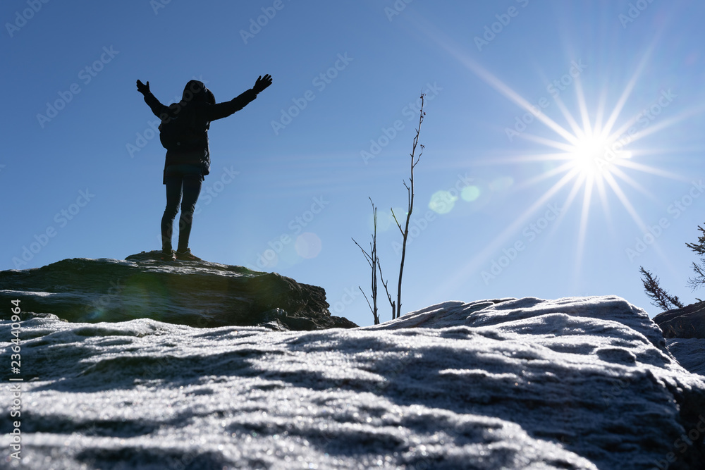 Cheering woman hiker open arms at mountain peak backlit with heavy lensflare and ice crystalls in the foreground. Cheering woman hiker open arms at mountain peak backlit with heavy lensflare and ice crystalls in the foreground.