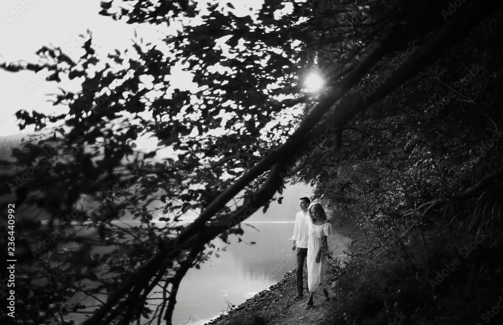 Fototapeta premium Young pretty couple hugging and smiling at the lake at sunset