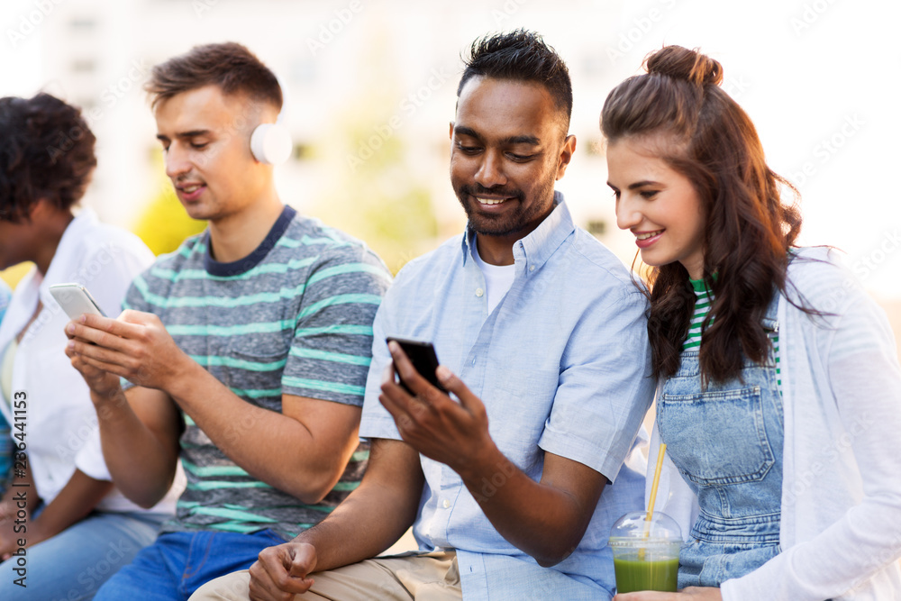 Obraz premium technology, friendship and international concept - group of friends with smartphones hanging out in summer city
