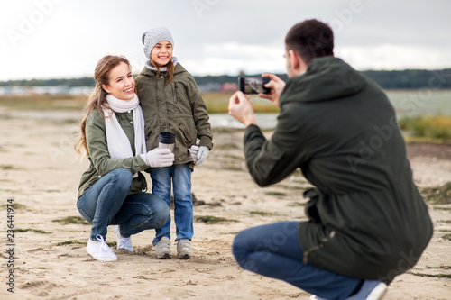 family, leisure and people concept - happy mother, father and little daughter photographing by smartphone on autumn beach