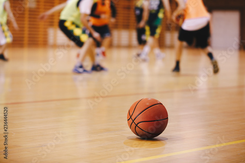 Basketball Training Game Background. Basketball on Wooden Court Floor Close Up with Blurred Players Playing Basketball Game in the Background © matimix