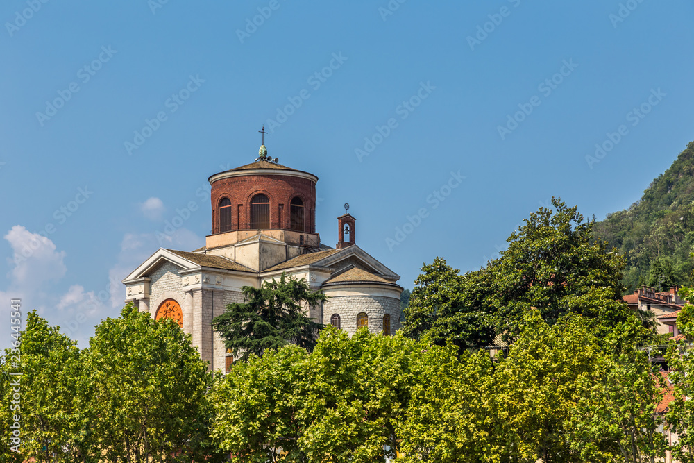View of Saint Ambroggio church, Laveno, Italy, against a blue sky, and surrounded by trees.