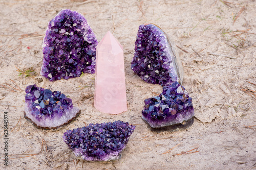 1 rose quartz gemstone surround by 5 amethyst crystals laying on the beach and in the grass photo