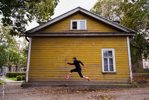 Dynamic athlete jumping in front of a yellow wood house photo