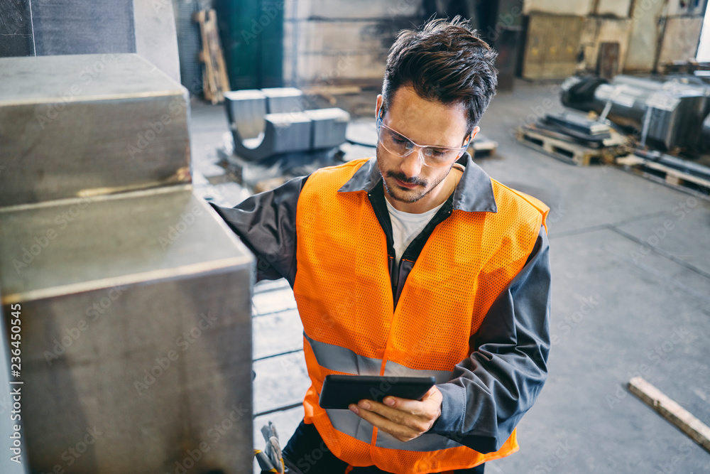 Man with tablet wearing protective workwear working in factory