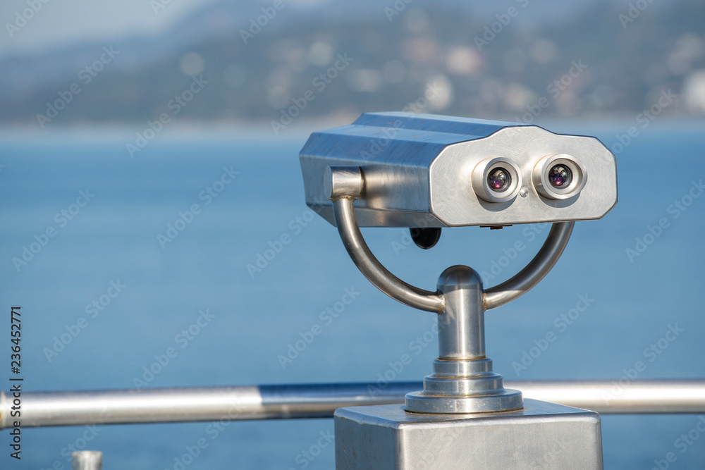 Public binocular on sea shore, close up. Coin operated binocular viewer on blurred background of sunset and sea Public binocular on sea shore, close up. Coin operated binocular viewer on blurred background of sunset and sea