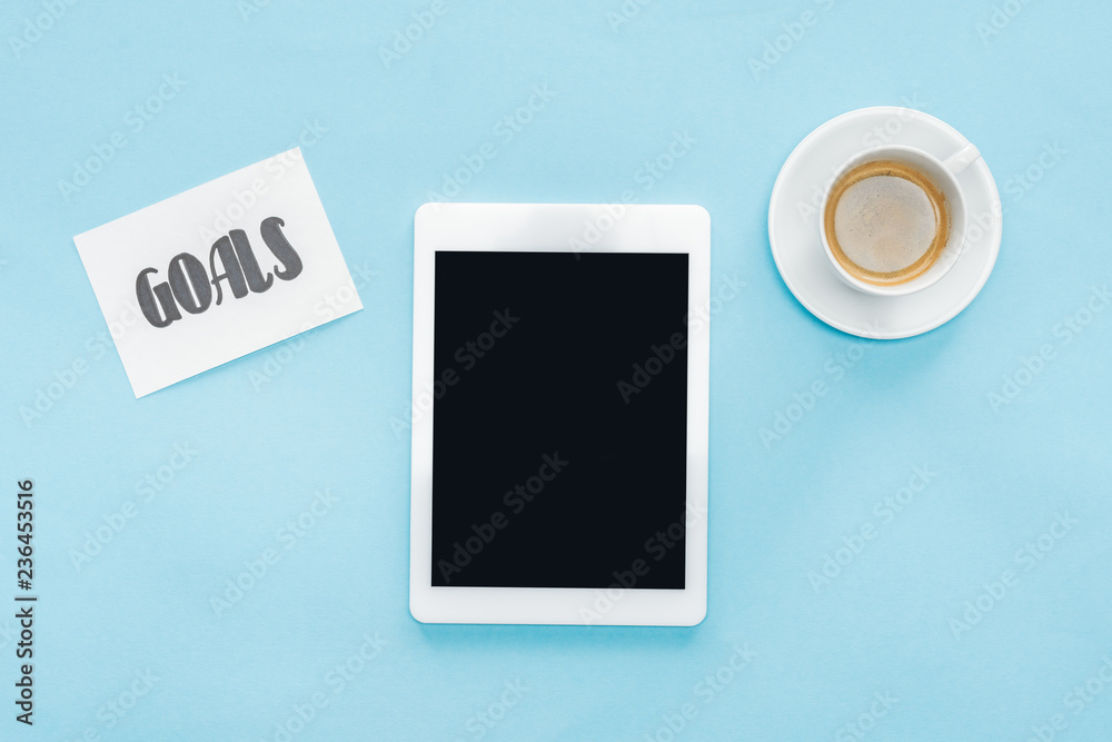 top view of digital tablet with blank screen, 'goals' lettering on card and coffee with blue background top view of digital tablet with blank screen, 'goals' lettering on card and coffee with blue background