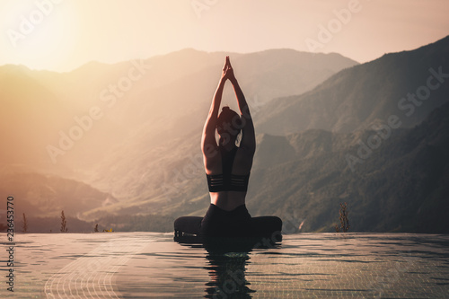 Fototapeta Naklejka Na Ścianę i Meble -  Beautiful Attractive Asian woman practice yoga Lotus pose on the pool above the Mountain peak in the morning in front of beautiful nature views,Feel so comfortable and relax in holiday,Warm tone