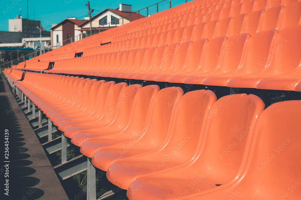 Naklejka premium the rows of chairs of orange color leaving in the distance, the tinted photo, plastic seats for the audience under