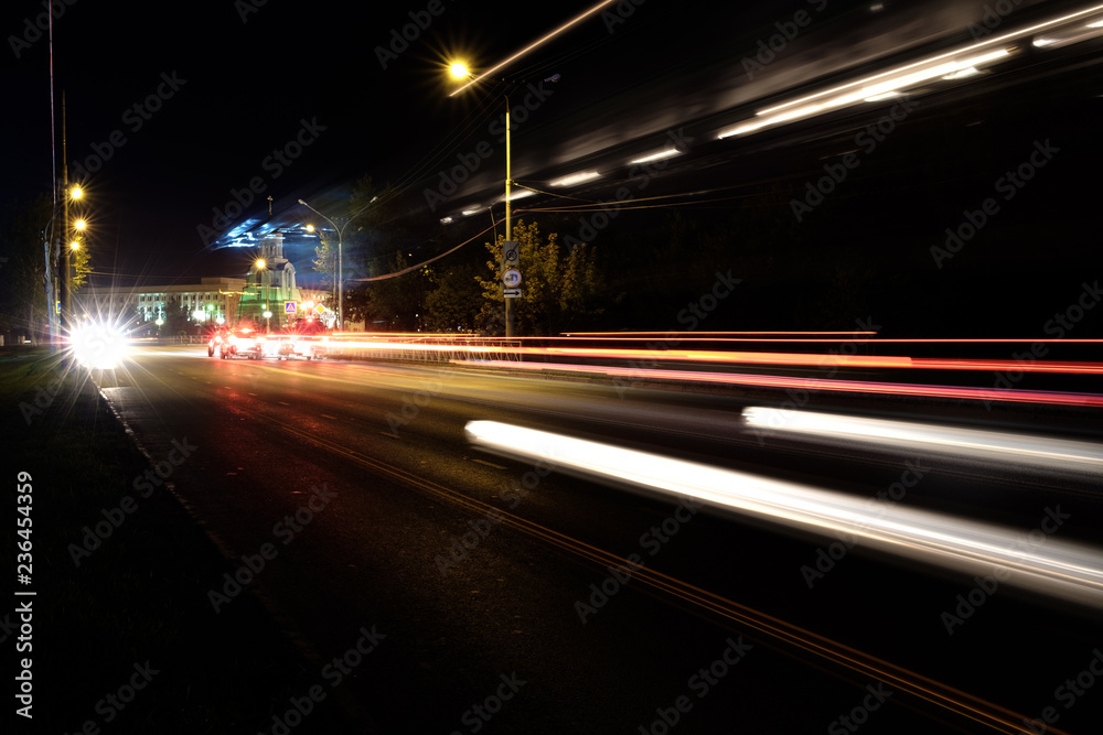 night road along the edges of the road there are lighting poles in the foreground traces of passing cars