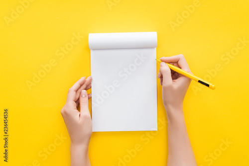  partial view person holding pen over blank notebook on yellow background photo