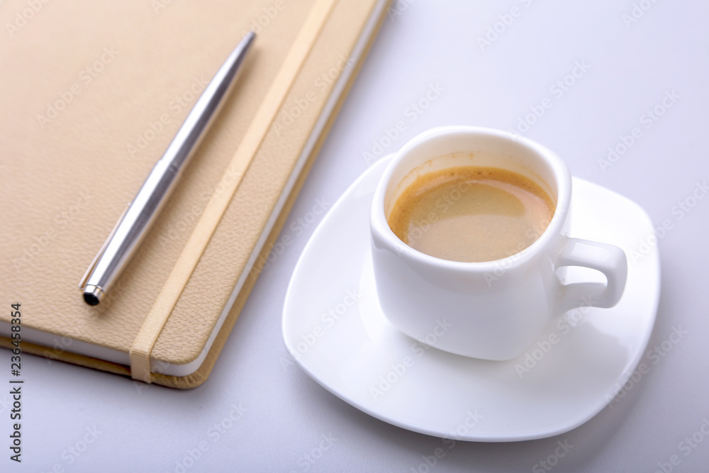 stylish notebook, ballpoint pen and white cup with a fragrant espresso coffee on the office desk. stylish notebook, ballpoint pen and white cup with a fragrant espresso coffee on the office desk.
