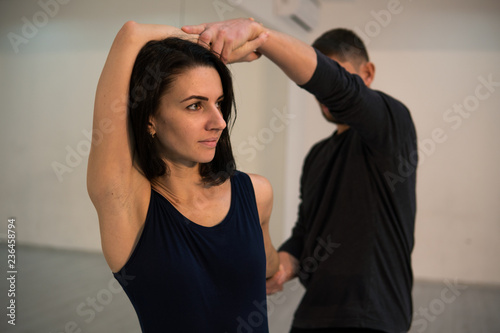 Young athletic couple in dark suits practicing pair yoga in studio with mirrors. Balancing in pair