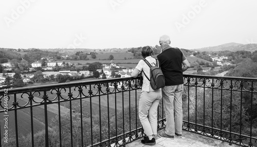  Senior couple (back view; unrecognizable) admiring view of Nive river valley from Cambo-les-Bains (a charming spa town) promenade. Springtime. French Basque country, France. Black and white photo.