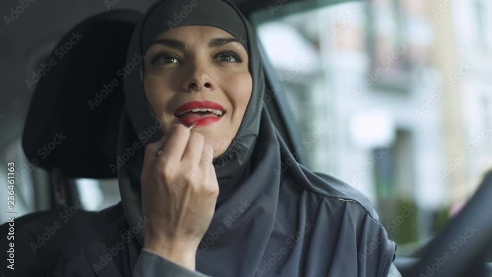 Attractive sexy lady in hijab applying red lipstick in automobile feminism, kiss