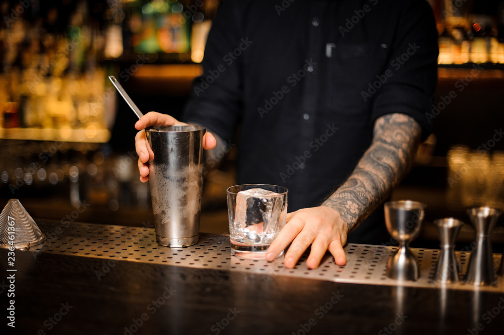 Bartender holding a glass with ice cube and steel shaker