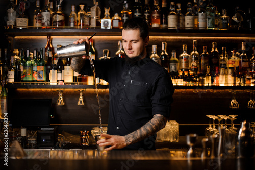 Professional bartender pouring the cocktail from the steel shaker
