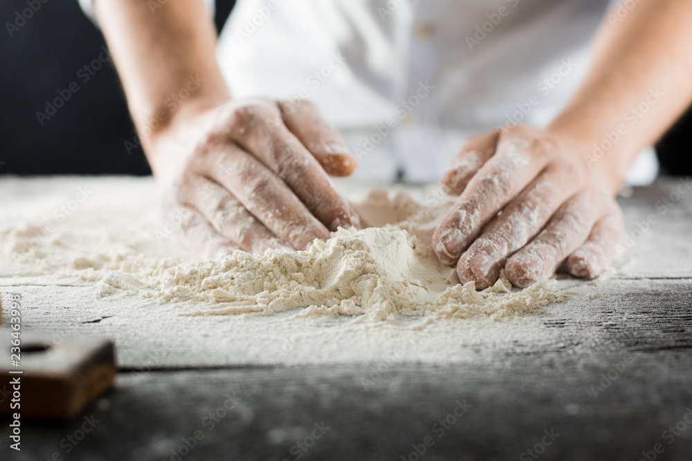 Male chef hands knead the dough with flour on the kitchen table
