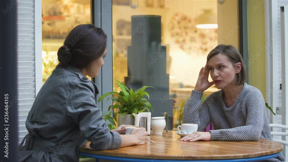 Two friends sitting in cafe, discussing family problems, lady comforting sister Two friends sitting in cafe, discussing family problems, lady comforting sister