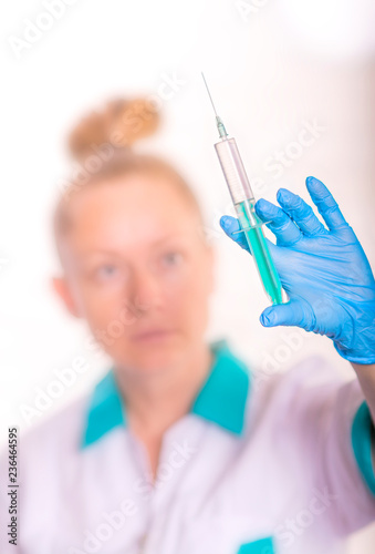 Doctor in latex gloves holding a syringe. Blurred background.