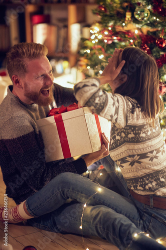 romantic surprise holiday – Cheerful man and woman with gift enjoying together on Christmas eve.