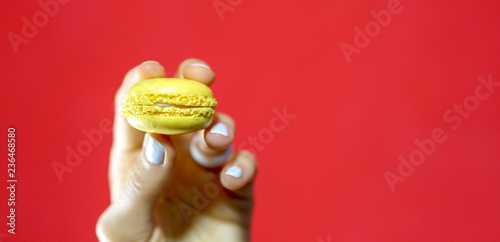Female hand hold a yellow lemon macaroon over red