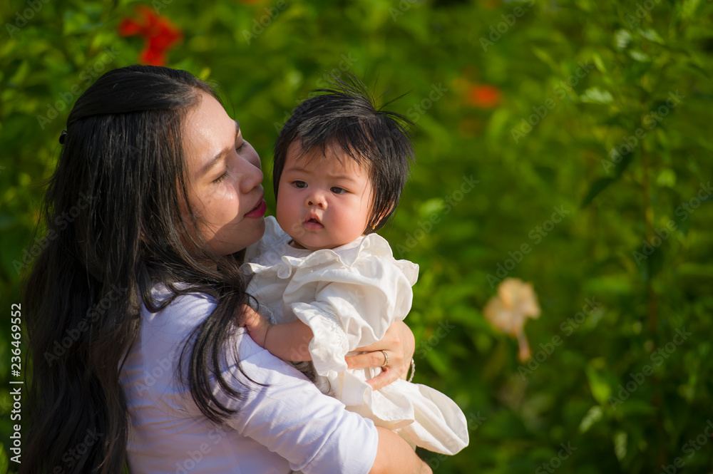 young happy and cute Asian Chinese woman enjoying and playing with her baby girl daughter holding and kissing her smiling cheerful at garden resort young happy and cute Asian Chinese woman enjoying and playing with her baby girl daughter holding and kissing her smiling cheerful at garden resort