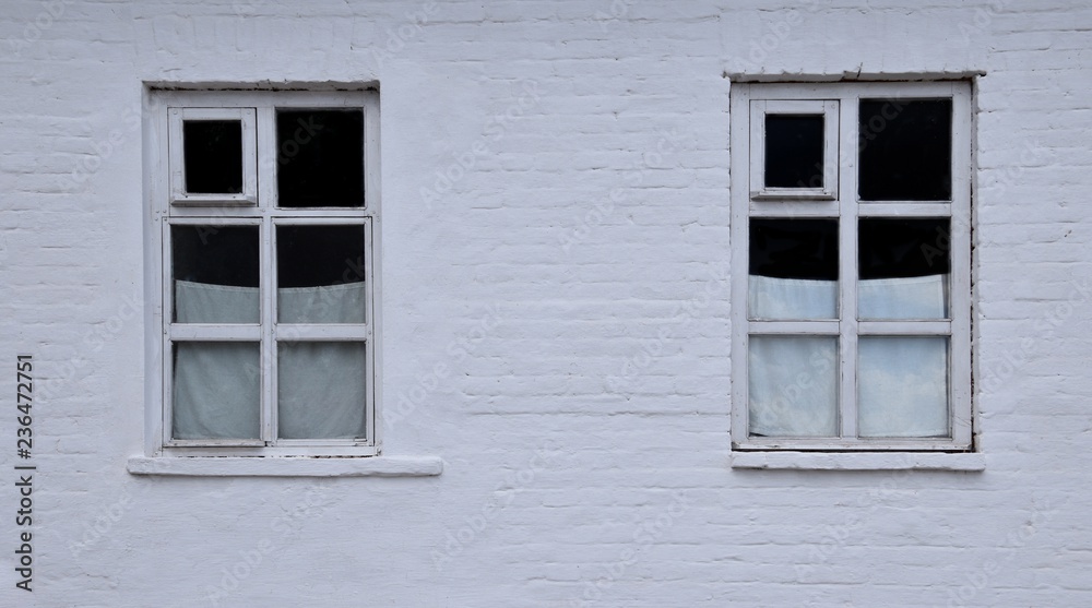 Two small city windows in a white brick wall with cute home curtains.