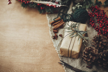 Stylish rustic christmas gift box with green branch and fir branches, berries, anise, pine cones, cinnamon on rustic wooden background. Simple eco present. Atmospheric mood. Space for text