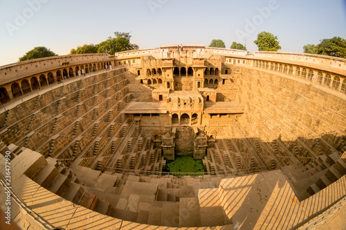 Fisheye shot of the abhaneri stepwell in jaipur rajasthan. Shows the steps, the palace and the green water with all the details of the beautiful stepwell, the surrounding area and the blue sky photo
