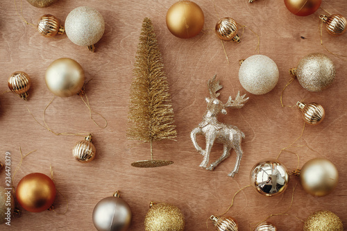 Merry Christmas. Christmas golden glitter tree with reindeer and shiny baubles and balls on rustic wooden background, flat lay. Modern gold decorations and present. Seasons greetings.