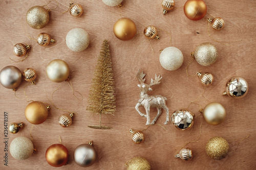 Christmas golden glitter tree with reindeer and shiny baubles and balls on rustic wooden background, flat lay. Modern gold decorations and present. Seasons greetings. Merry Christmas