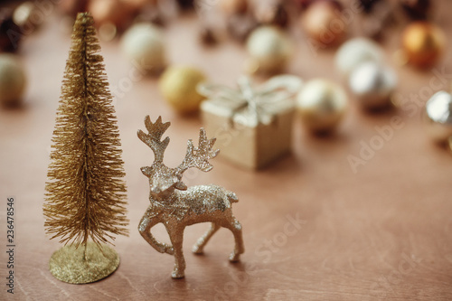 Fototapeta Naklejka Na Ścianę i Meble -  Christmas golden glitter tree and reindeer on background of gift box, shiny baubles and balls on rustic background. Modern gold decorations and present. Seasons greetings. Merry Christmas