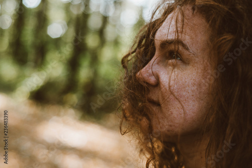 Autumn closeup portrait of a ginger girl in forest with leaves in hair, fall. Beautiful girl.