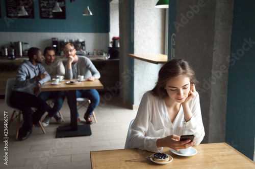 Diverse young guys interested with beautiful girl sitting at near table using smartphone, enjoying coffee in cafe, curious males looking at pretty female, liking or falling in love from first sight