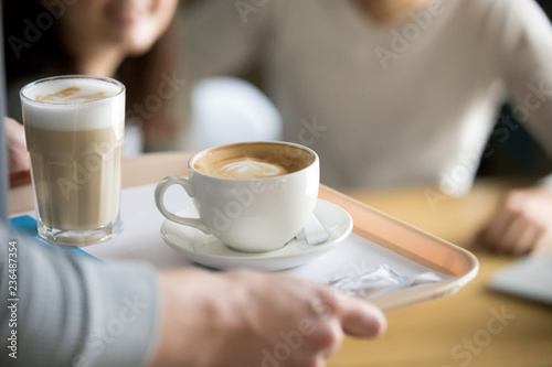 Close up of waiter holding aromatic cappuccino and latte on tray bringing order to cafe guests, coffeeshop worker give hot drinks to visitors, cups with delicious fresh brewed coffee on platter