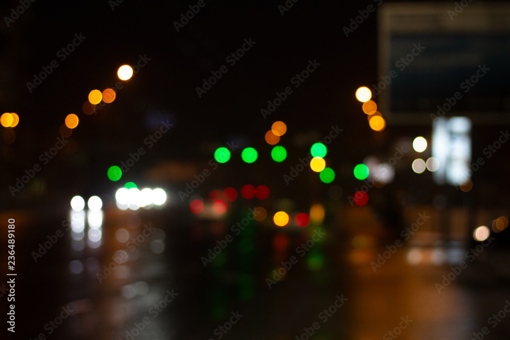 Lanterns of the night city illuminate the road. Blurred photo with defocus. Headlights of cars in the night city. Multicolored bright festive night lights bokeh.