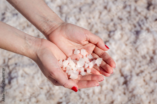 Female hand holding natural salt crystals on the background of a salt lake view from above