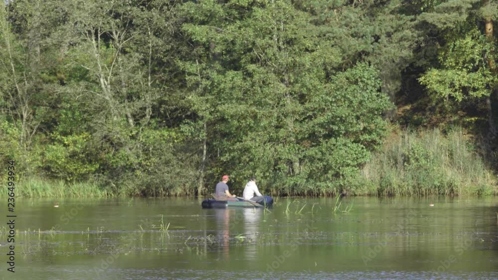 Two fisherman in rubber boat floats rowing with oars on river. Man is fishing on lake in sunny forest. Stracha river - beautiful place close to Belarusian nuclear power plant Two fisherman in rubber boat floats rowing with oars on river. Man is fishing on lake in sunny forest. Stracha river - beautiful place close to Belarusian nuclear power plant