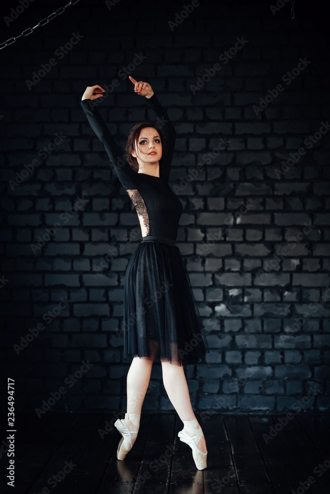 Ballerina in black dress and Pointe shoes in the background of a black brick wall. The room with the chains.
