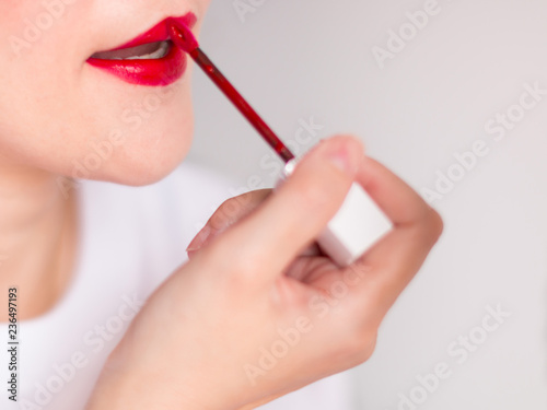 A hand of woman dyeing the lips with red lipstick.