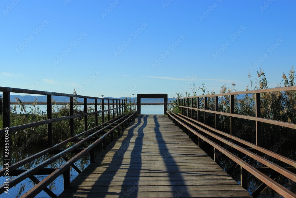Wooden boardwalk and bridge connecting two shores over a canal gate at the end view of the sea and mountains  at the background at koronisia village in Greece