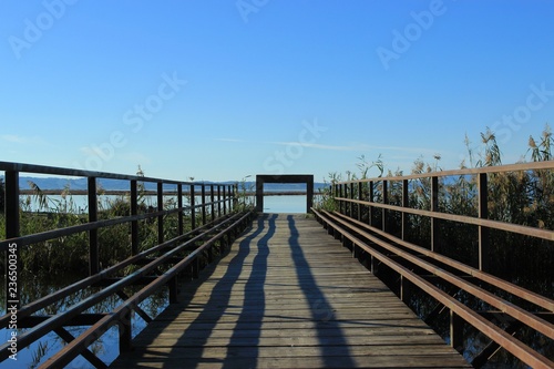 Wooden boardwalk and bridge connecting two shores over a canal gate at the end view of the sea and mountains  at the background at koronisia village in Greece