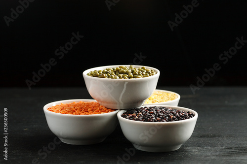 Set of different cereals and legumes in a white bowls on a black table