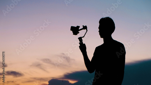 Silhouettes of a tourist man with a stabilizer and a video camera close up