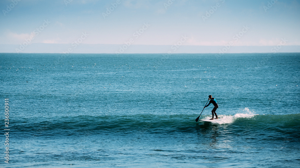 Silhouette of unidentifiable man castching a wave while on a stand up paddle board