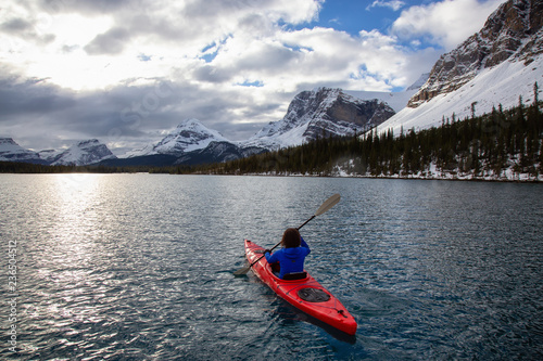 Adventurous girl kayaking in a glacier lake surrounded by the Canadian Rockies during a cloudy morning. Taken at Bow Lake, Banff, Alberta, Canada.