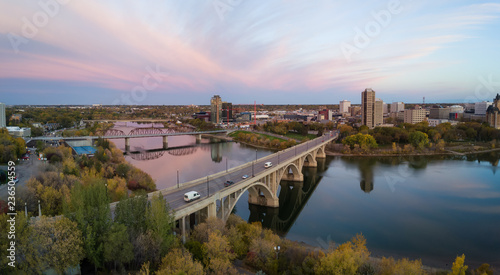 Aerial panoramic view of a bridge going over Saskatchewan River during a vibrant sunrise in the Fall Season. Taken in Saskatoon, SK, Canada.