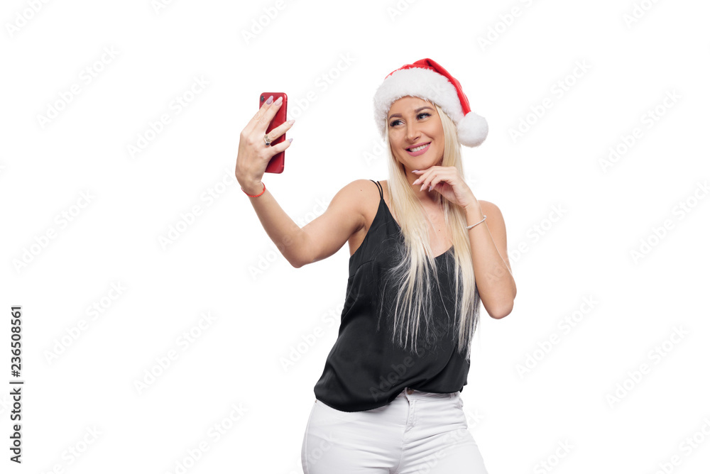 Smiling happy blond woman in black blouse and christmas santa hat make selfie on red smartphone camera over isolated white background. Sale concept Smiling happy blond woman in black blouse and christmas santa hat make selfie on red smartphone camera over isolated white background. Sale concept