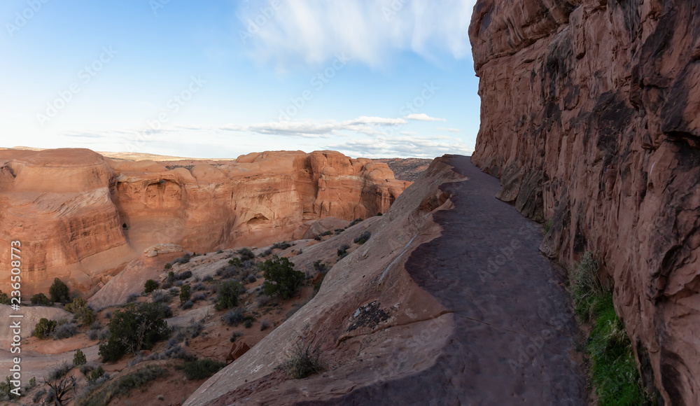 Obraz premium Scenic path near a dangerous cliff on a mountain during a vibrant sunny day before sunset. Taken in Arches National Park, located near Moab, Utah, United States.